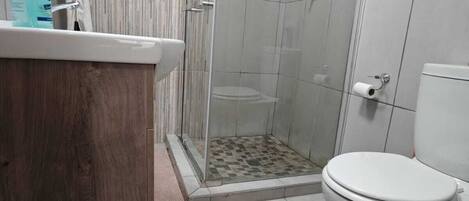 A bathroom with a shower, toilet, and a wooden vanity.
