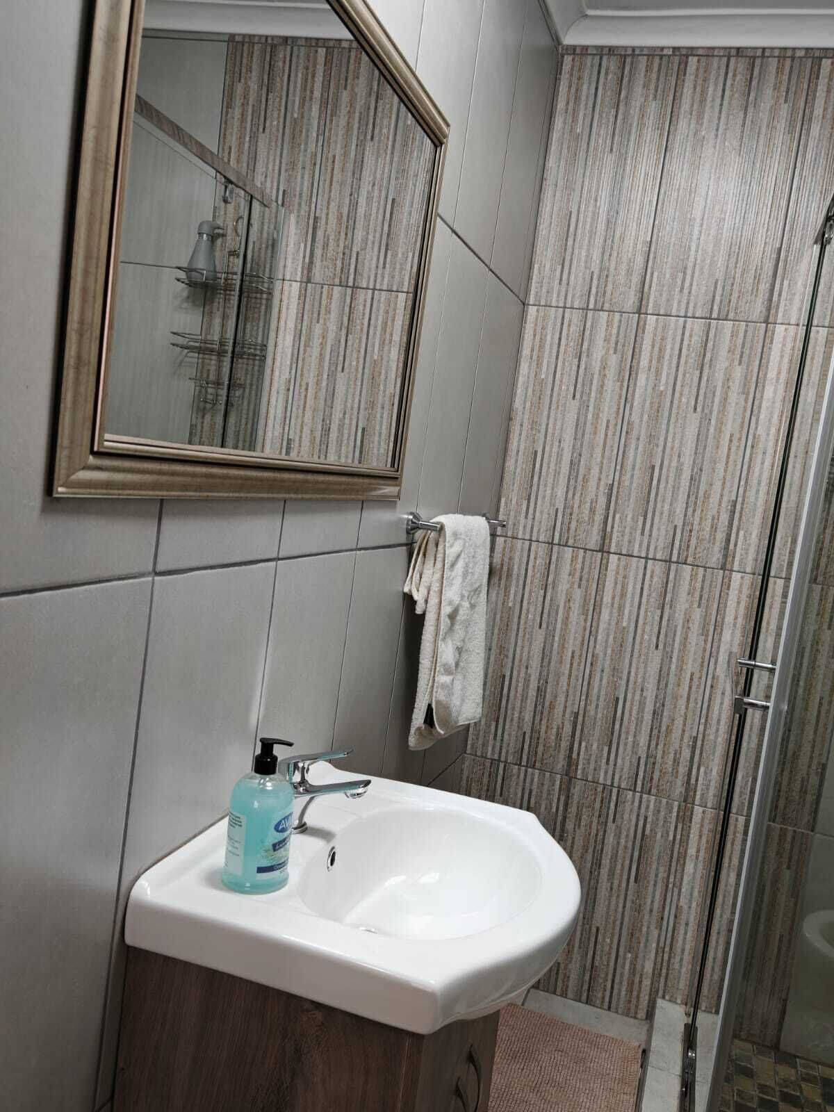 Un baño con lavamanos blanco, espejo y zona de ducha.