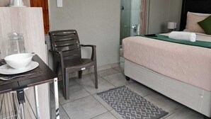 A hotel room with a bed, a chair, a table with a bowl and cups, and a shower area. - Zondiles Guesthouse  (MP)