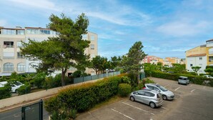 Un parking avec plusieurs voitures, une clôture verte et des bâtiments en arrière-plan.