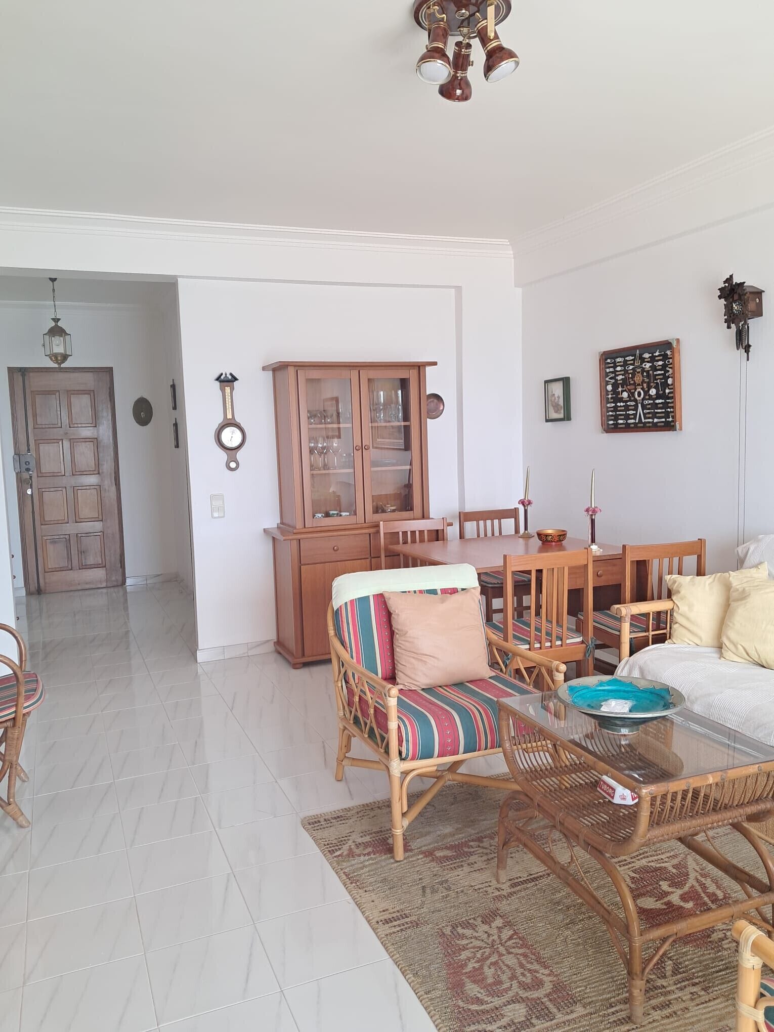 A living room with a dining table, chairs, a sofa, a wooden cabinet, and a clock on the wall.