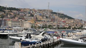 A marina with boats docked, a pier, and a cityscape with buildings in the background. - Lofts with beach (Napoli)