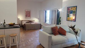 A modern living room with a sofa, a dining area with stools, a bed, and artwork on the walls. - Lofts with beach (Napoli)