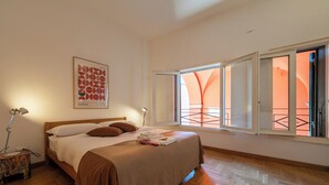 A bedroom with a bed, a nightstand, a lamp, a window with an orange view, and a wall art piece. - Lofts with beach (Napoli)