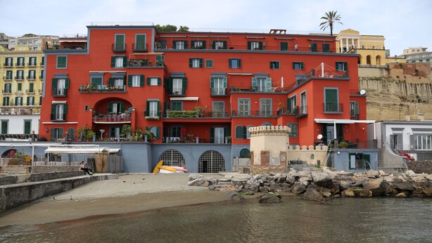 A multi-story building with balconies, a beach in the foreground, and a rocky shoreline. - Lofts with beach (Napoli)