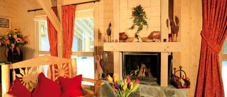 A wooden interior with a fireplace, a bench with red cushions, a vase with flowers, and a wooden table.