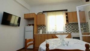 Eine kleine Küche mit Holzschränken, einem weißen Kühlschrank, einem Spülbecken und einem Esstisch mit Stühlen.