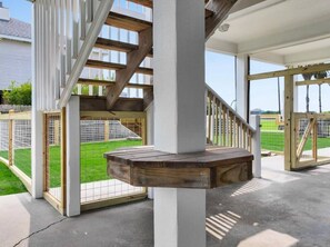 Ein überdachter Außenbereich mit einer hölzernen Bank, einer Treppe und Blick auf einen umzäunten Garten.