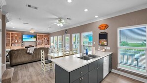 A modern kitchen with a central island, built-in cabinetry, and a dining area with a sofa and chairs. - Ocean Views Hear The Waves Sleeps 8 Walk to Beach (Bolivar Peninsula)