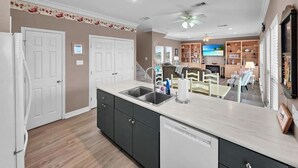A modern kitchen with a dishwasher, double sink, and a dining area with a table and chairs. - Ocean Views Hear The Waves Sleeps 8 Walk to Beach (Bolivar Peninsula)