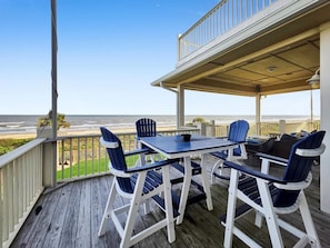 Eine überdachte Terrasse im Freien mit Tisch und Stühlen, mit Blick auf einen Strand.