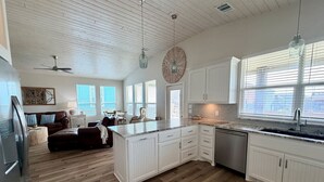 A spacious kitchen with white cabinetry, a large island, and a dining area with a brown leather sofa. - Ocean View•New Build • sleeps 9• Fenced Yard (Bolivar Peninsula)