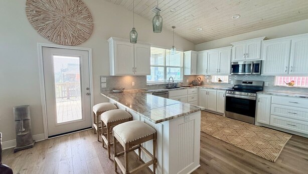 A modern kitchen with white cabinetry, a large island with stools, and a view through the door. - Ocean View•New Build • sleeps 9• Fenced Yard (Bolivar Peninsula)