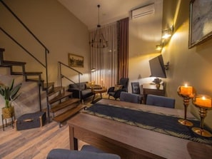 Een moderne woonkamer met een houten trap, een eettafel met stoelen en een kroonluchter.
