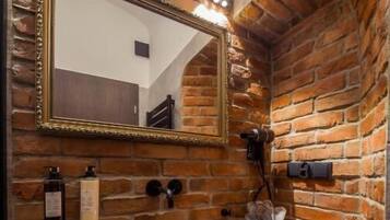 Un baño con tocador de madera, un lavabo negro, un espejo con marco dorado y una pared de ladrillo.