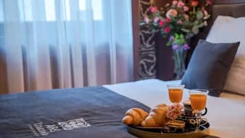 Una cama con una bandeja de cruasanes y jugo de naranja, un jarrón de flores y una colcha oscura con un logotipo.