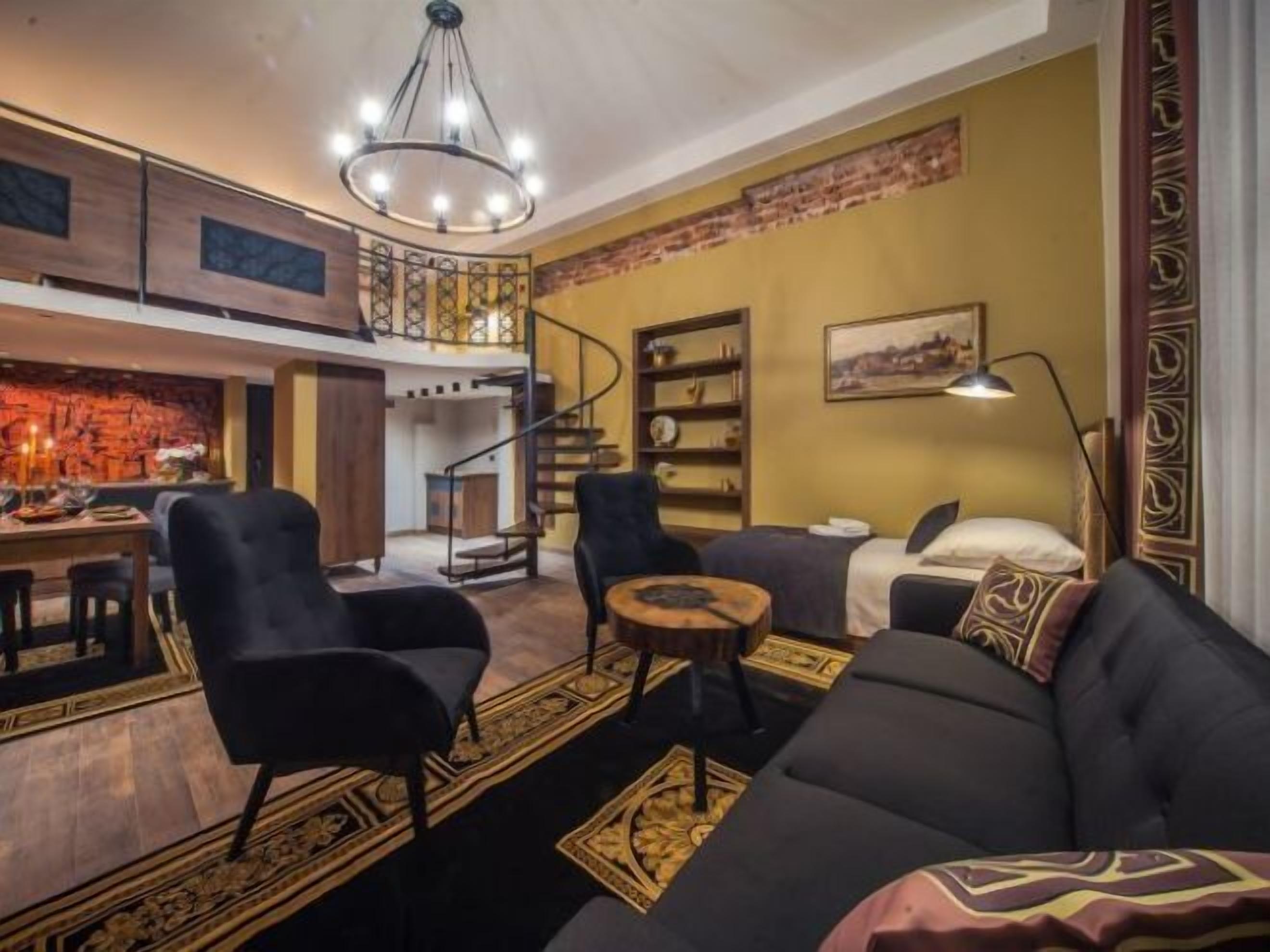 Een ruime woonkamer met een zwarte bank, twee fauteuils, een salontafel, en een eethoek met een bar.