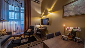 Una habitación de hotel moderna con sofá, mesa de comedor, sillas, televisor y un jarrón decorativo con flores.