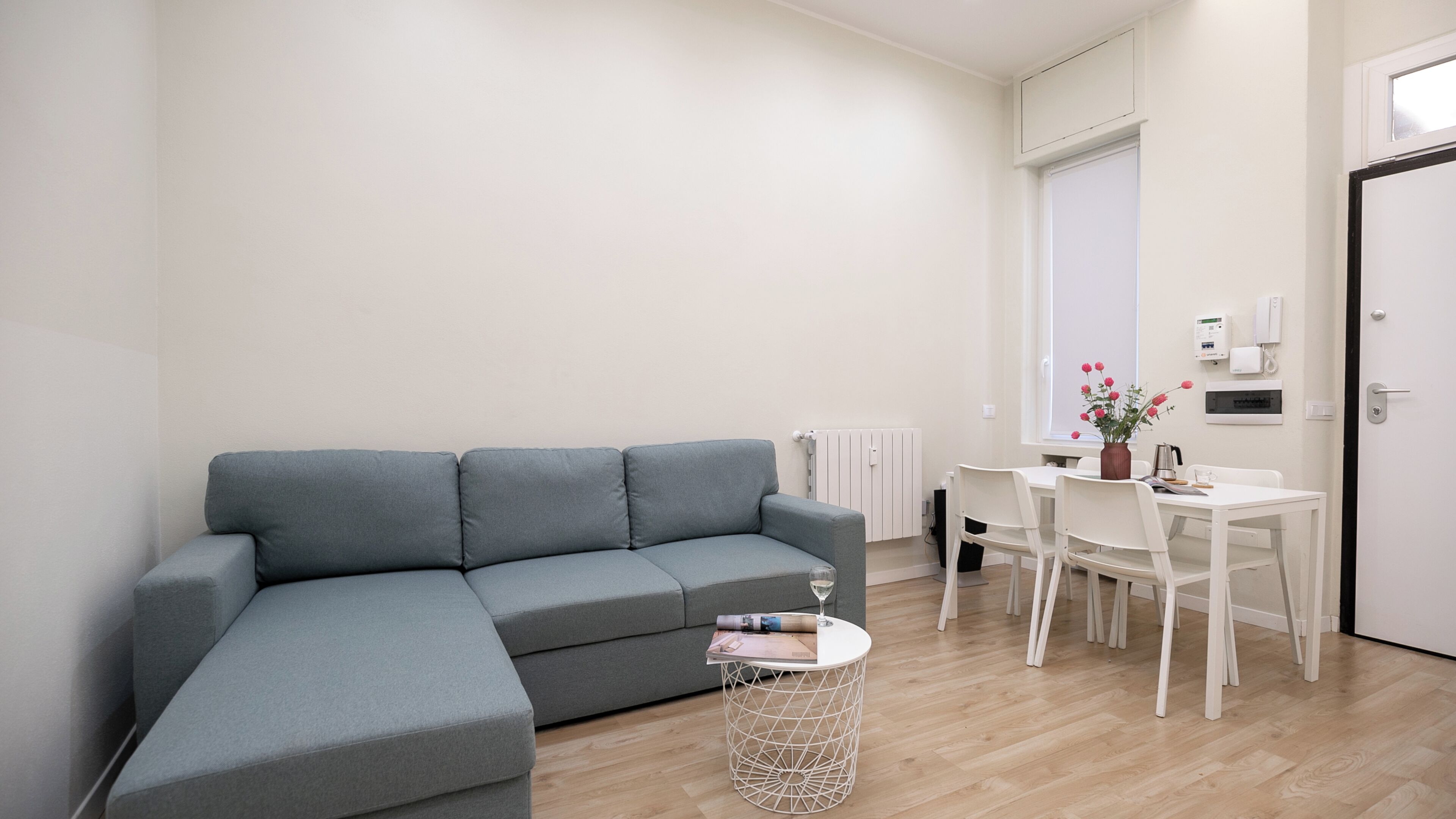 A modern living room with a grey sectional sofa, a round coffee table, and a dining area with a white table and chairs.