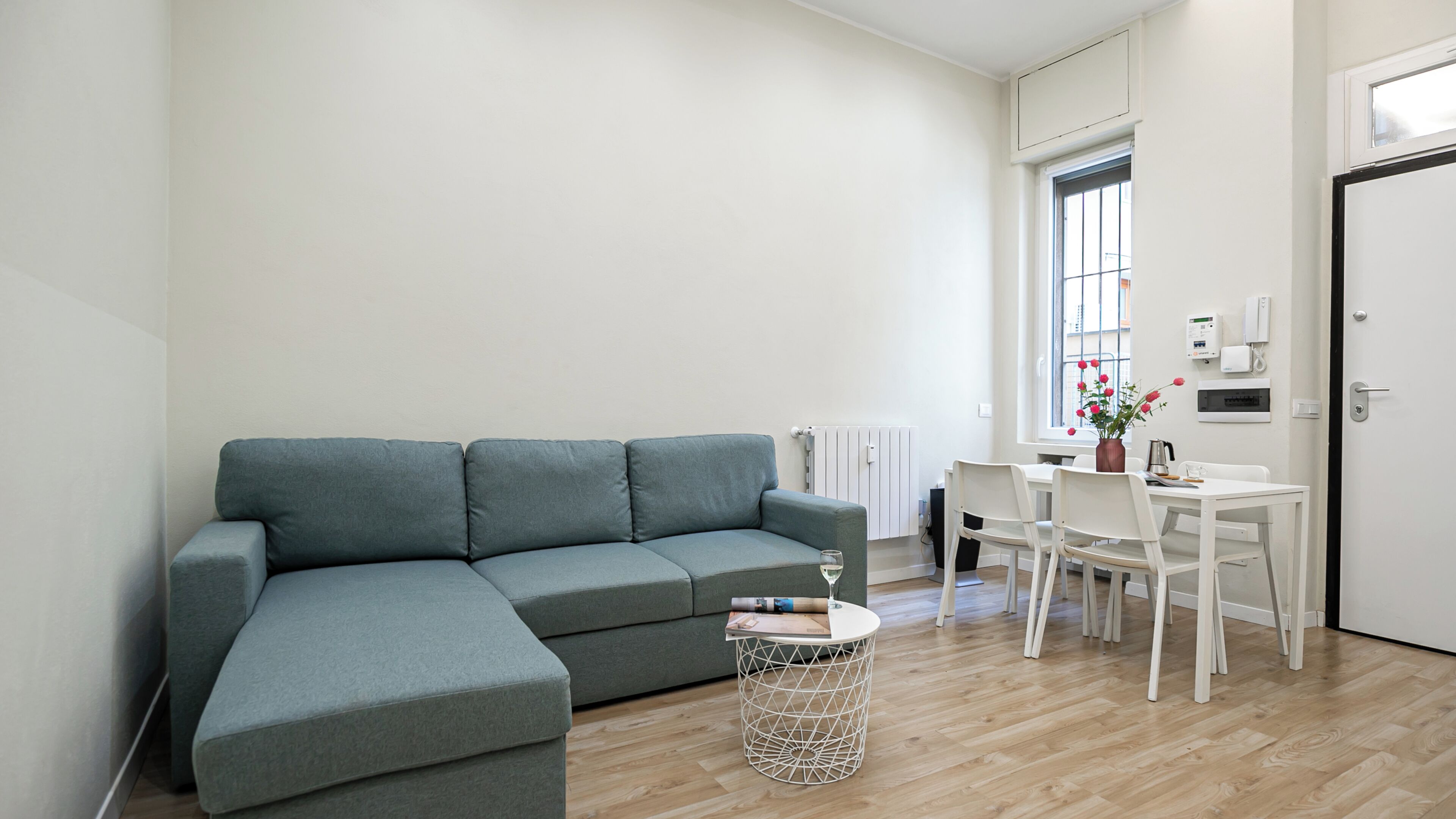 Una sala de estar con un sofá gris, una mesa de centro redonda y una zona de comedor con sillas blancas y una mesa.