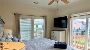 Una camera da letto con un letto, una televisione, una ventola a soffitto e un balcone con vista.