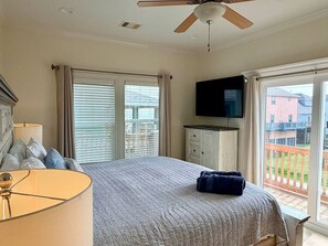 Ein Schlafzimmer mit Bett, Fernseher, Deckenventilator und einem Balkon mit Aussicht.