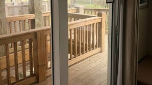 Una stanza con una porta scorrevole in vetro che dà su un pontile in legno con vista sulla spiaggia e sulle case.