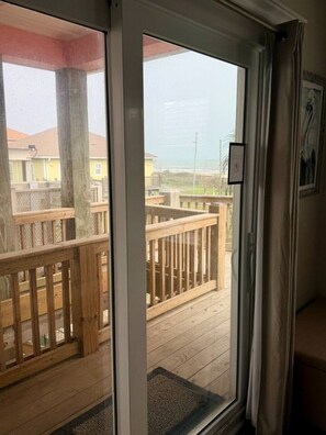 Ein Zimmer mit einer Schiebeglasdoor zur Holzterrasse, mit Blick auf Strand und Häuser.