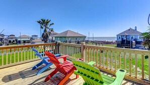 Un terrazzo in legno con poltrone Adirondack colorate, vista sull'oceano e case sullo sfondo.