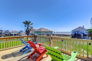 Eine Holzterrasse mit bunten Adirondack-Stühlen, Blick auf das Meer und Häuser im Hintergrund.