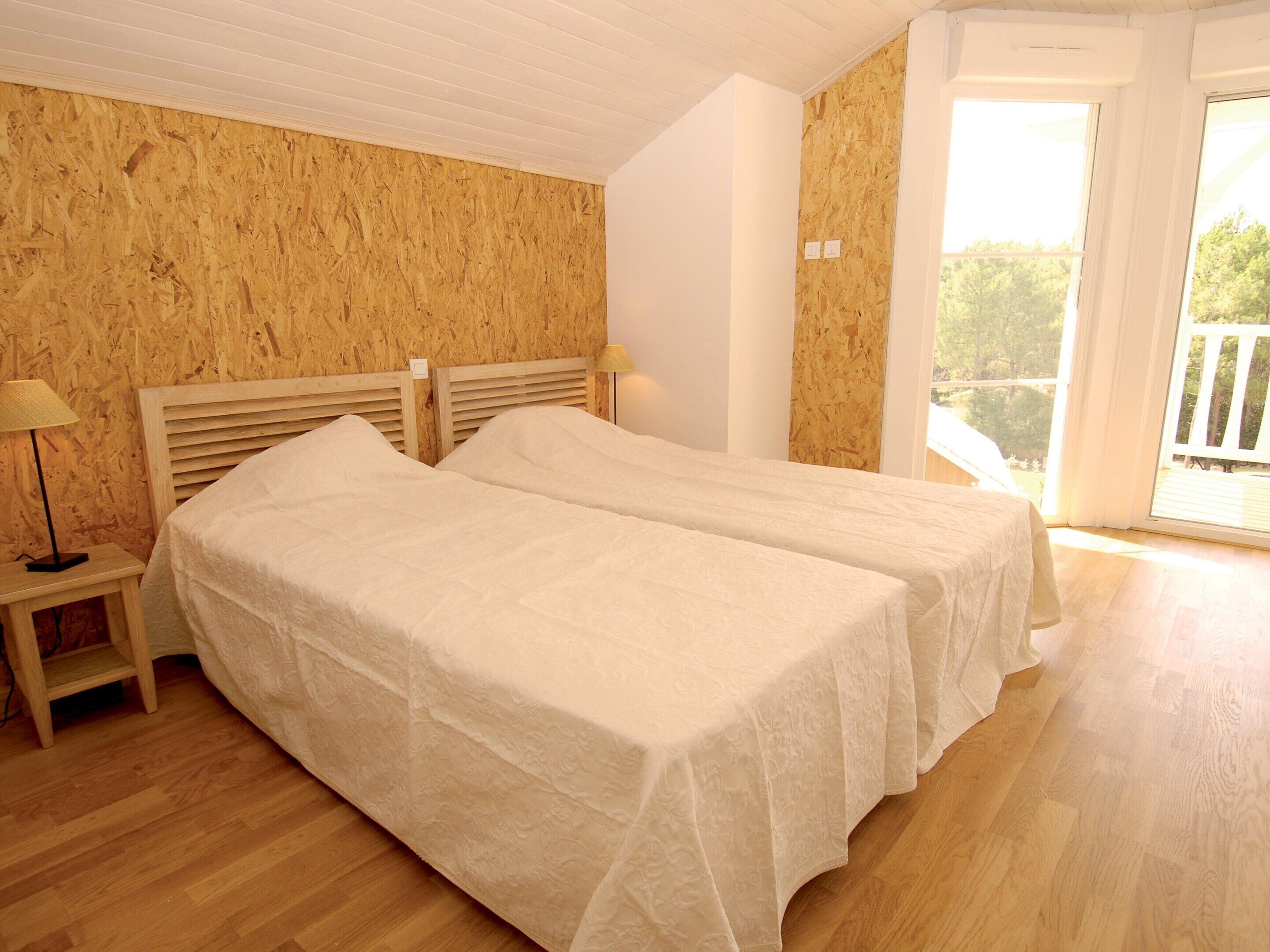 Una habitación con dos camas, suelo de madera, una mesita de noche con lámpara y un amplio ventanal con vistas.