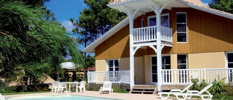 A two-story house with a balcony, a swimming pool, and outdoor furniture.