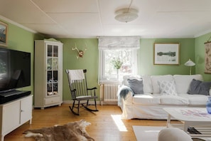 A living room with a television, a rocking chair, a white sofa, and a fur rug on the floor. - 3BR In Kosta - Fire pit, gathering room, Lake &Pub (Källeskruv)