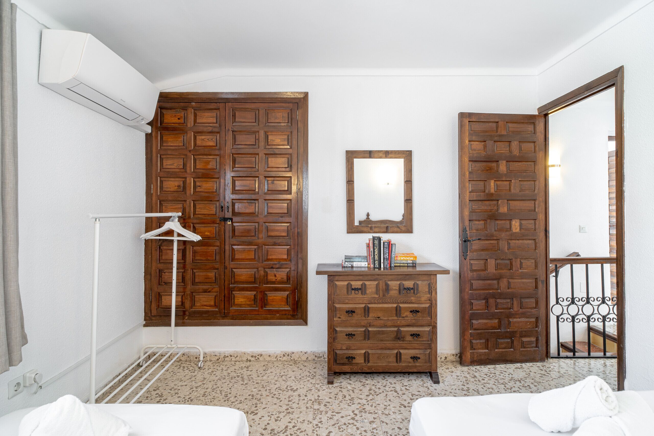 A hotel room with a wooden wardrobe, a mirror, a hanging clothes rack, and a bed.