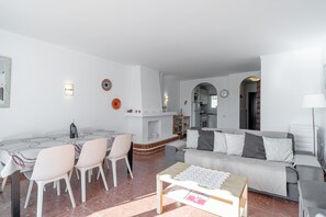 Ein Wohnzimmer mit einer Couch, einem Esstisch mit Stühlen, einem Kamin und einer Küche im Hintergrund.