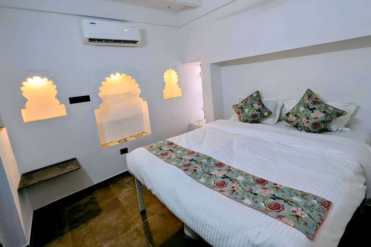 Un dormitorio con cama, luces decorativas en la pared, unidad de aire acondicionado y colcha con estampado floral.