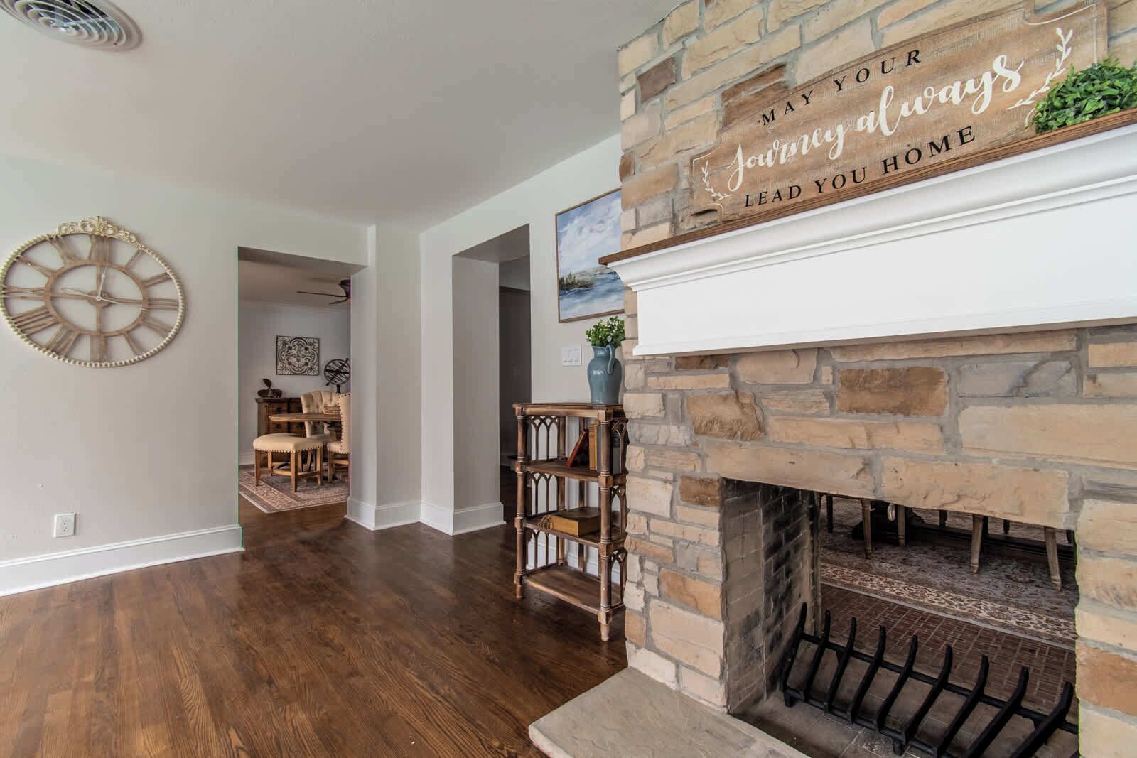 A spacious living room with a fireplace, a clock on the wall, and a sign above the fireplace.