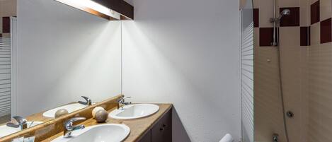 A bathroom with two sinks, a mirror, a towel rack, and a shower.