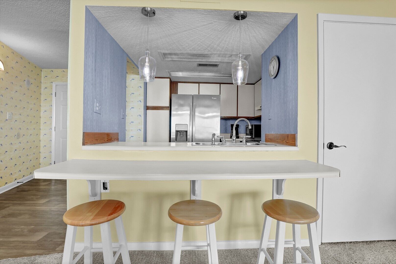 A kitchen with a white countertop, stainless steel appliances, and three wooden stools.