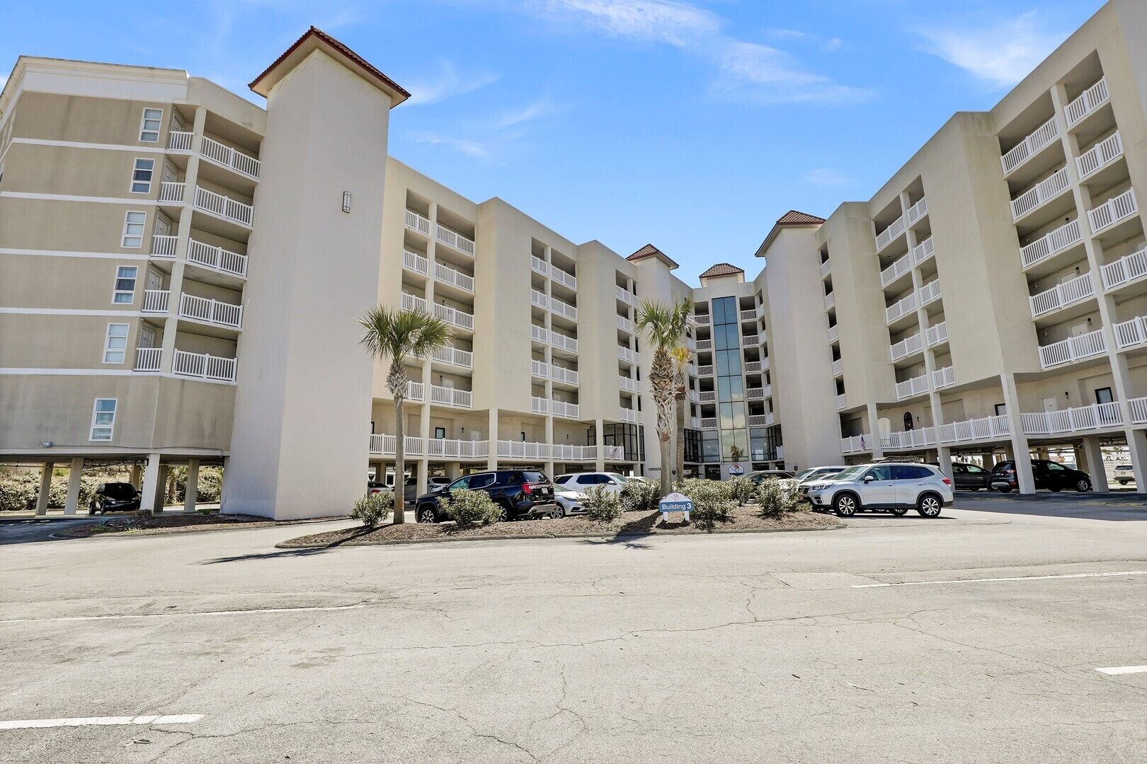 A multi-story hotel with balconies, parking, and a clear sky.