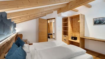 Une chambre avec un plafond en pente, des poutres en bois, un lit avec du linge de lit blanc, une armoire en bois et une petite table de chevet.
