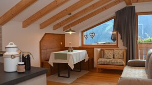 Una habitación acogedora con techo de madera, una mesa con mantel blanco, un sofá y una ventana con vistas al verdor.