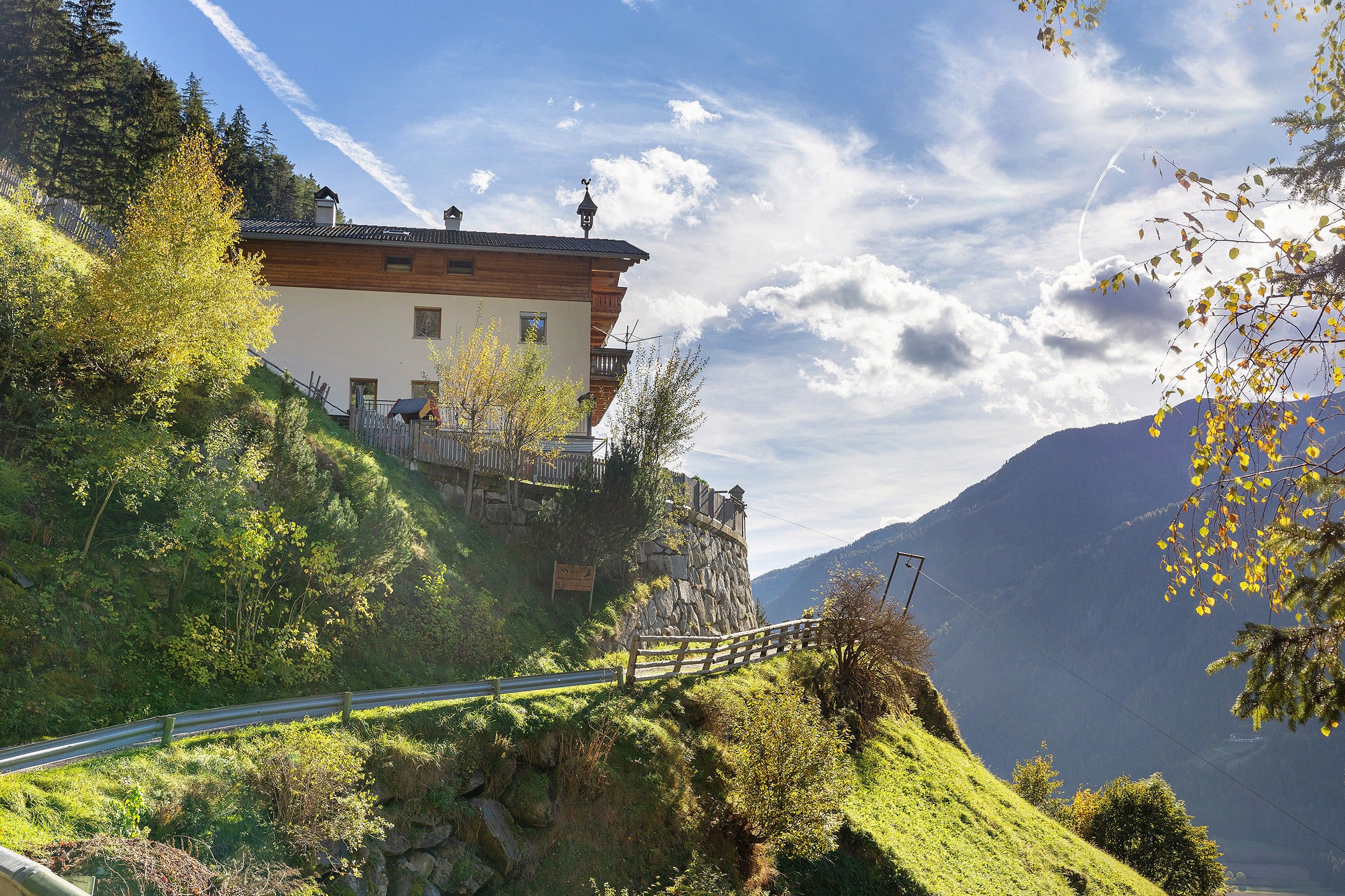 A mountain house with a wooden fence, a stone wall, and a clear sky.