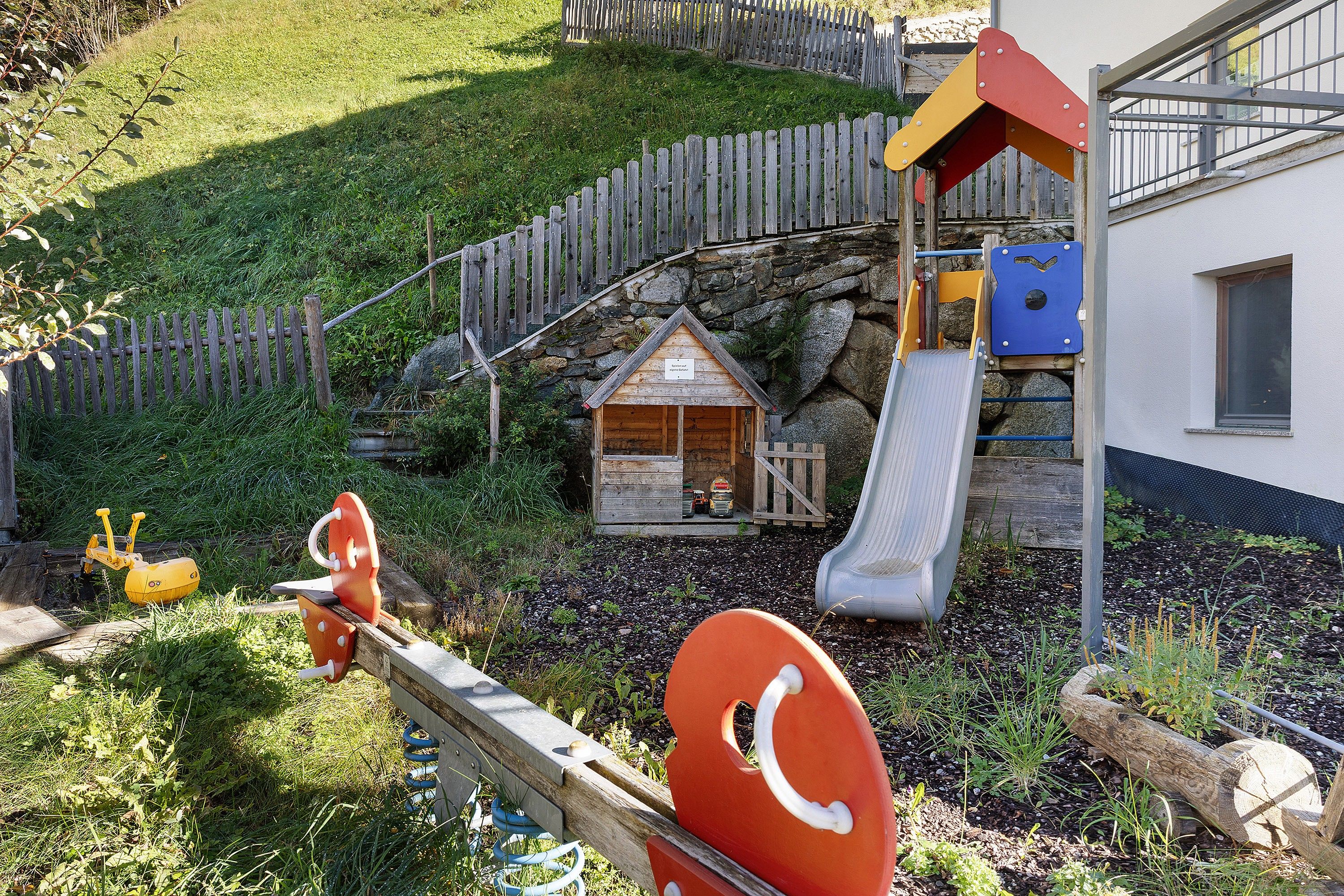 Un’area giochi con uno scivolo, altalene e una piccola struttura in legno.