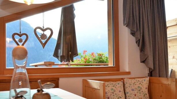 Una habitación con una cama de madera, una mesa con objetos decorativos, una ventana con vistas a montañas y una cortina.