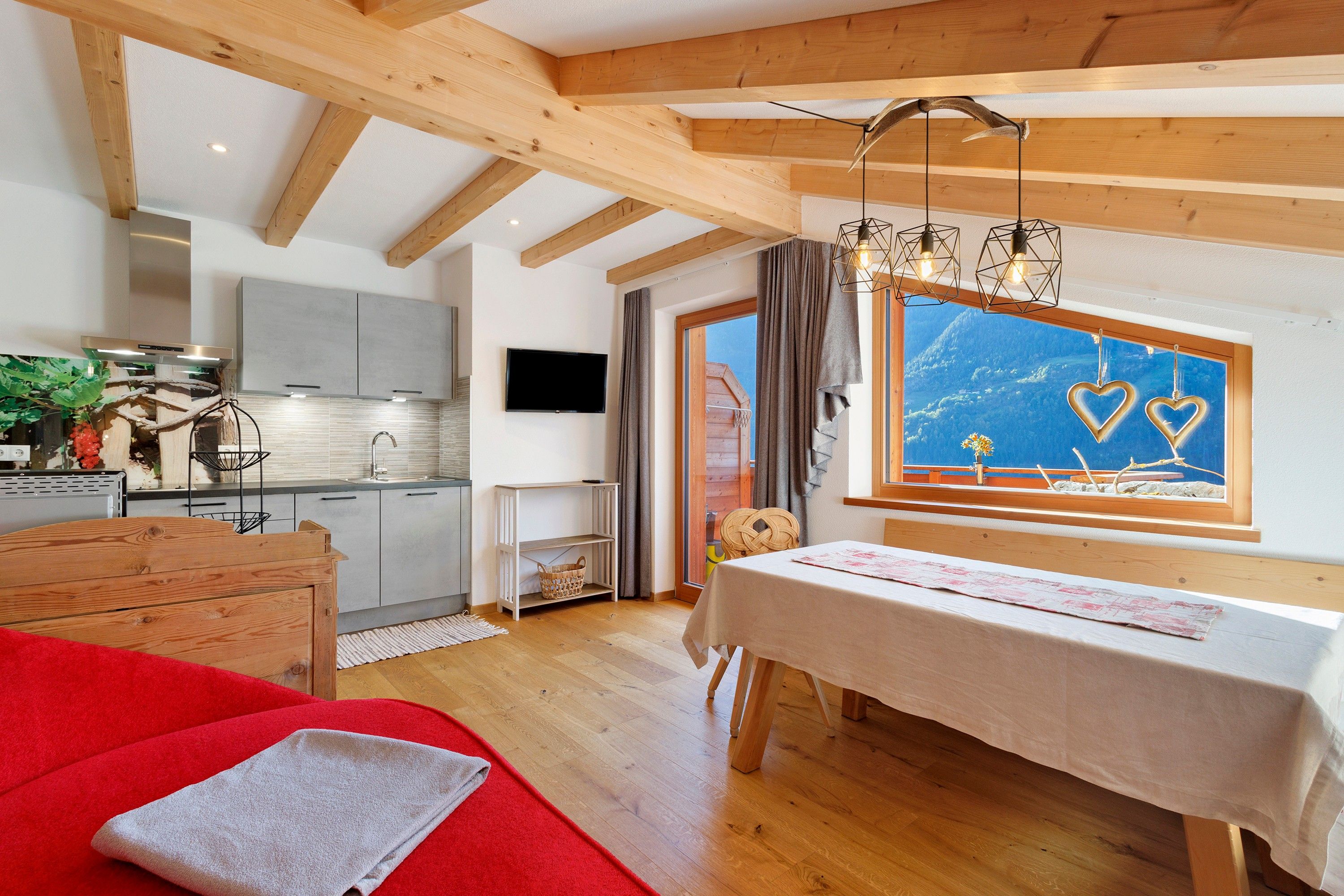 Een gezellige kamer met een houten plafond, een eettafel met een wit tafelkleed en een raam met uitzicht op de lucht en bergen.