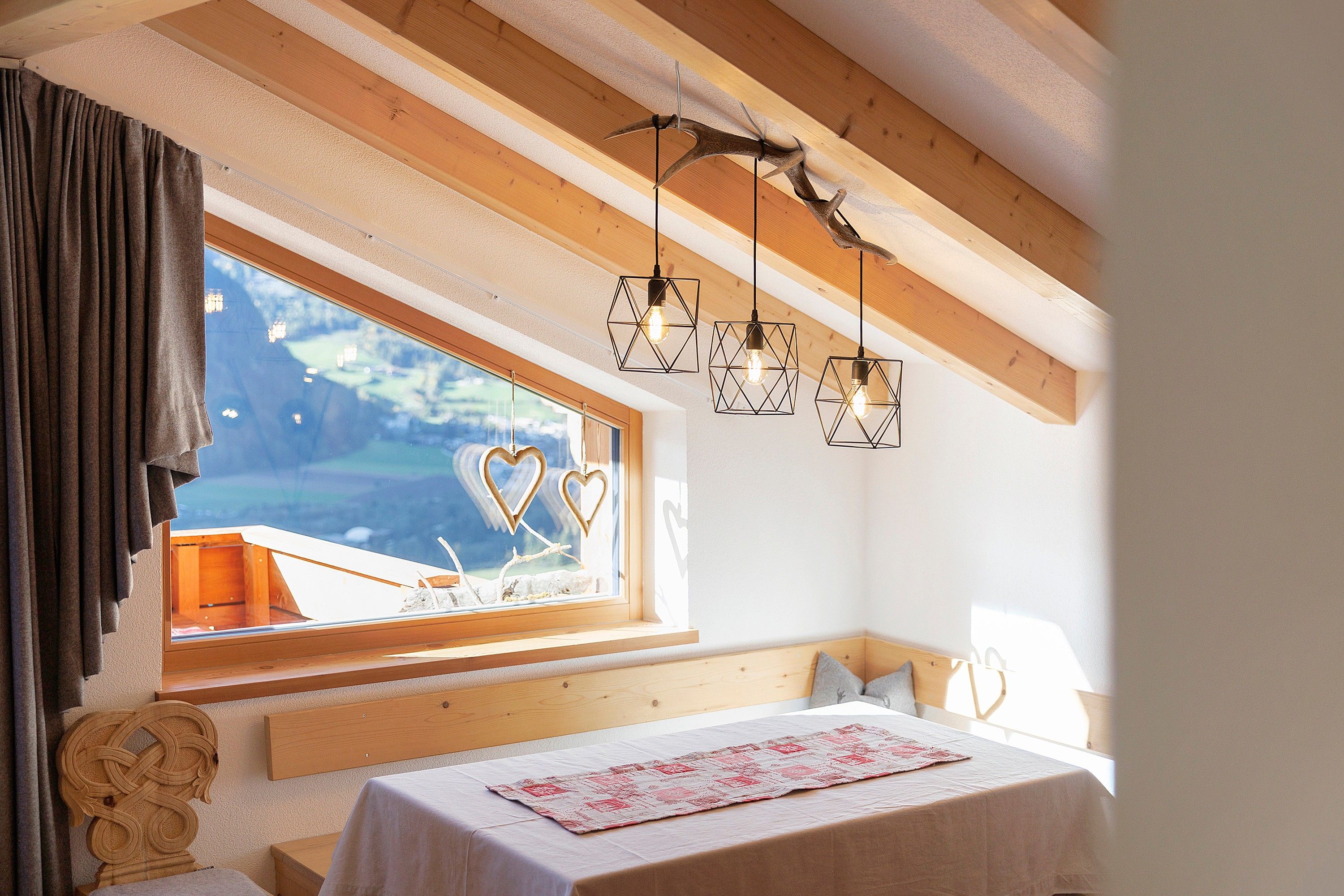 Een slaapkamer met een houten hoofdbord, een raam met gordijnen, een bed met een witte dekbedovertrek en geometrische hanglampen.