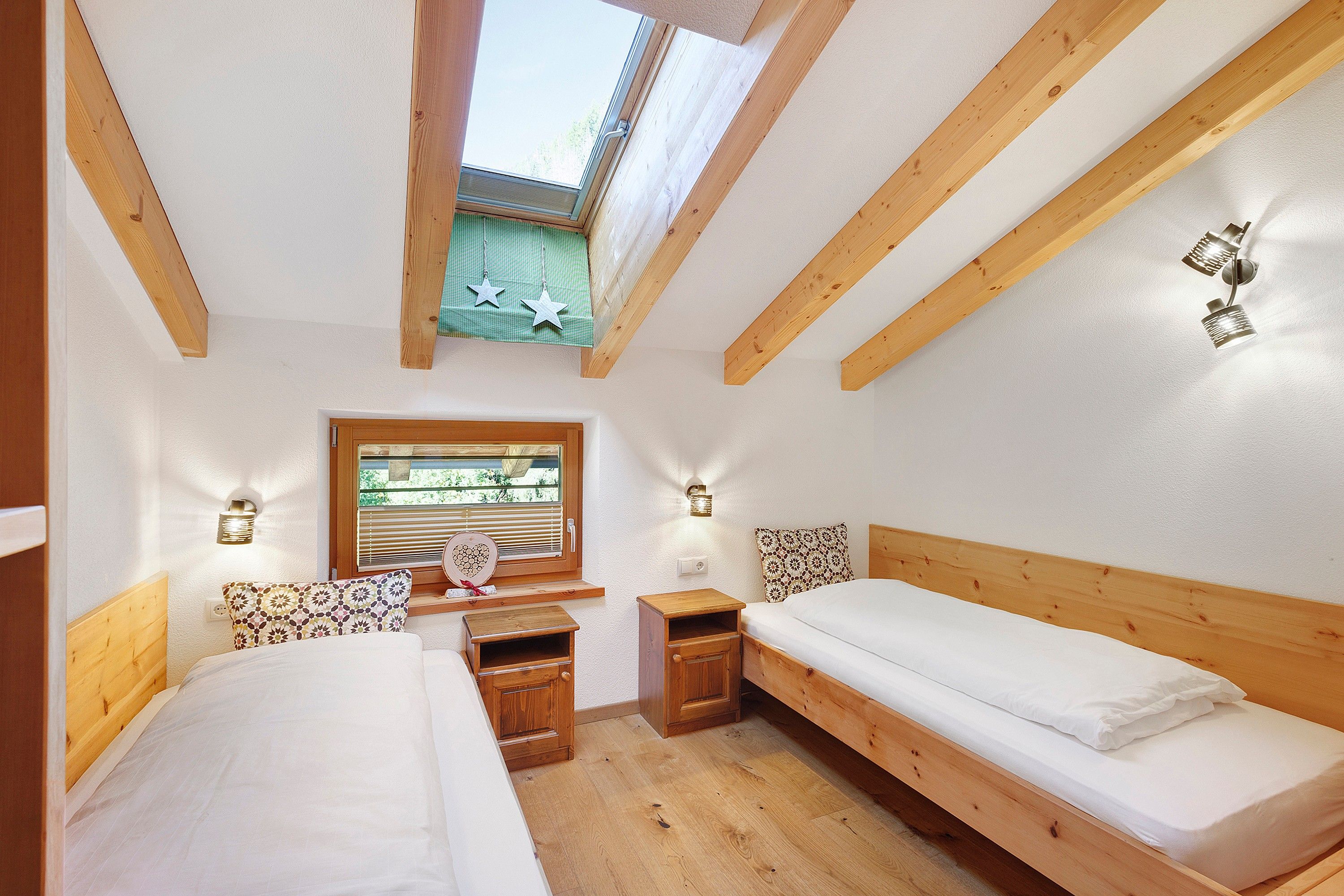 Una habitación con dos camas, una ventana con persianas, una mesita y una lámpara fijada a la pared.