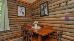 L’intérieur d’un chalet en bois, avec une table à manger, des chaises, des affiches encadrées et une décoration suspendue.