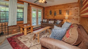 L’intérieur d’une cabane en rondins, avec un plafond en bois, un ventilateur de plafond, un canapé, un banc et une table.
